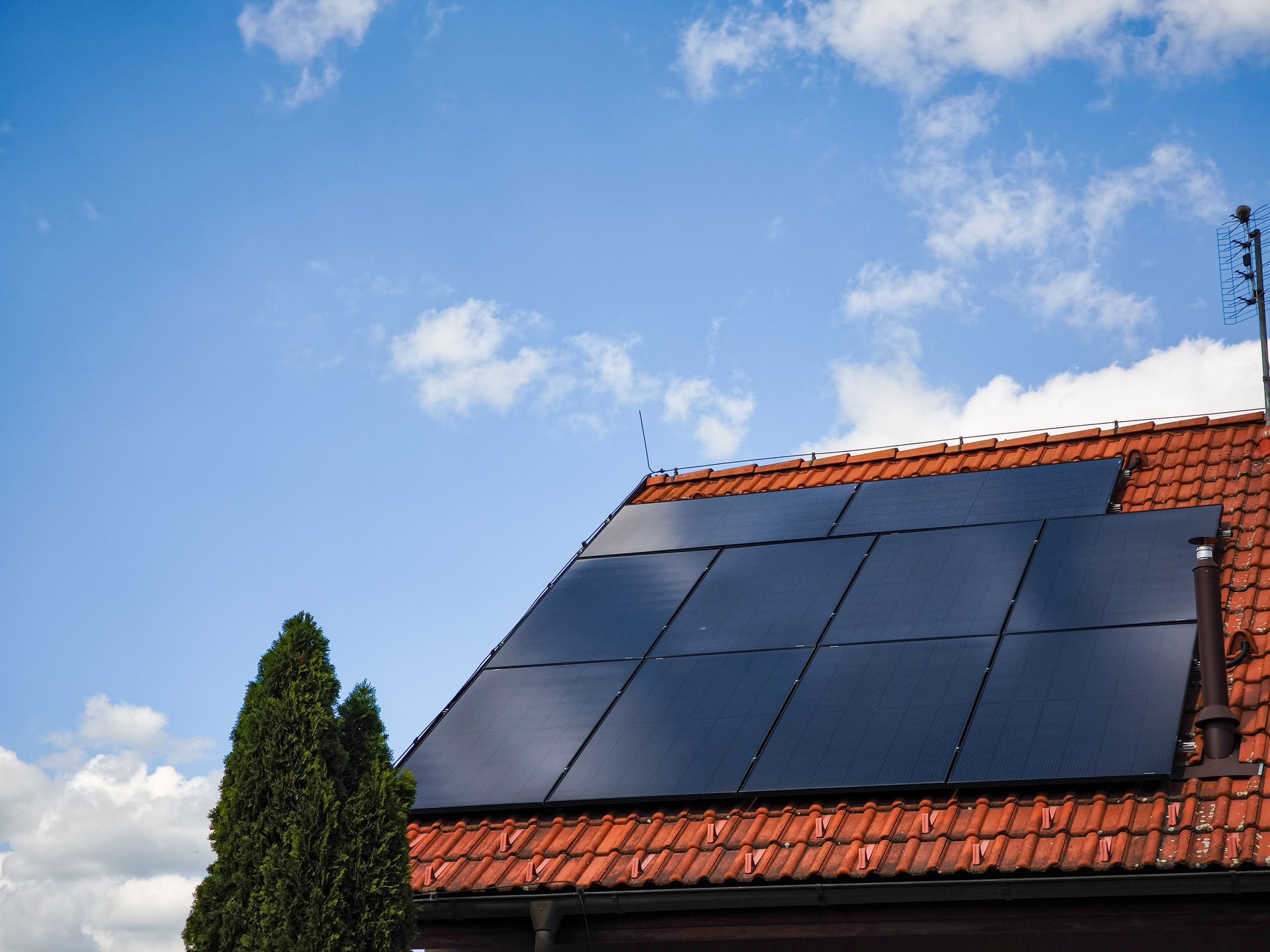 Solar panels installed on a residential roof under a bright blue sky with fluffy clouds showcasing renewable energy technology and sustainability concept